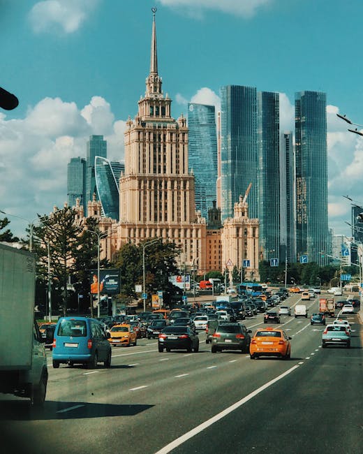 The image depicts a busy urban street scene with multiple vehicles, including cars and taxis, driving along a multi-lane road. In the background, there is a prominent historical building with an ornat