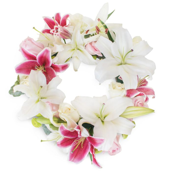 Radiating reverence and beauty, this circular floral wreath features a striking blend of white Oriental lilies and deep fuchsia-pink Stargazer lilies, each bloom perfectly balanced against a crisp white background. The lilies, some stately and open, their petals curving outward to reveal gentle green stamens, and others still budding with promise, bring a sense of purity and tranquillity to the arrangement. Interwoven are luscious blush pink and creamy white roses, their form ranging from tightly wound buds to softly ruffled, open faces, adding dimension and romantic softness to the design. Delicate, silvery-green foliage-possibly eucalyptus or lily leaves-lines the wreath, peeking between the blooms to offer fresh contrast and an earthy undertone. This lush, abundant circle is skillfully crafted by South Tottenham's expert florists, capturing the spirit of compassionate gatherings along Philip Lane or in the quiet corners of Lordship Recreation Ground. The meticulous composition forms an endless loop, symbolising the cycle of remembrance and life's enduring beauty. Perfect for solemn occasions such as funerals or celebrations of life, this wreath stands out as a heartfelt tribute, evoking comfort and shared memory within the South Tottenham neighbourhood, crafted for delivery with care by professionals who serve the area with commitment and artistry.
